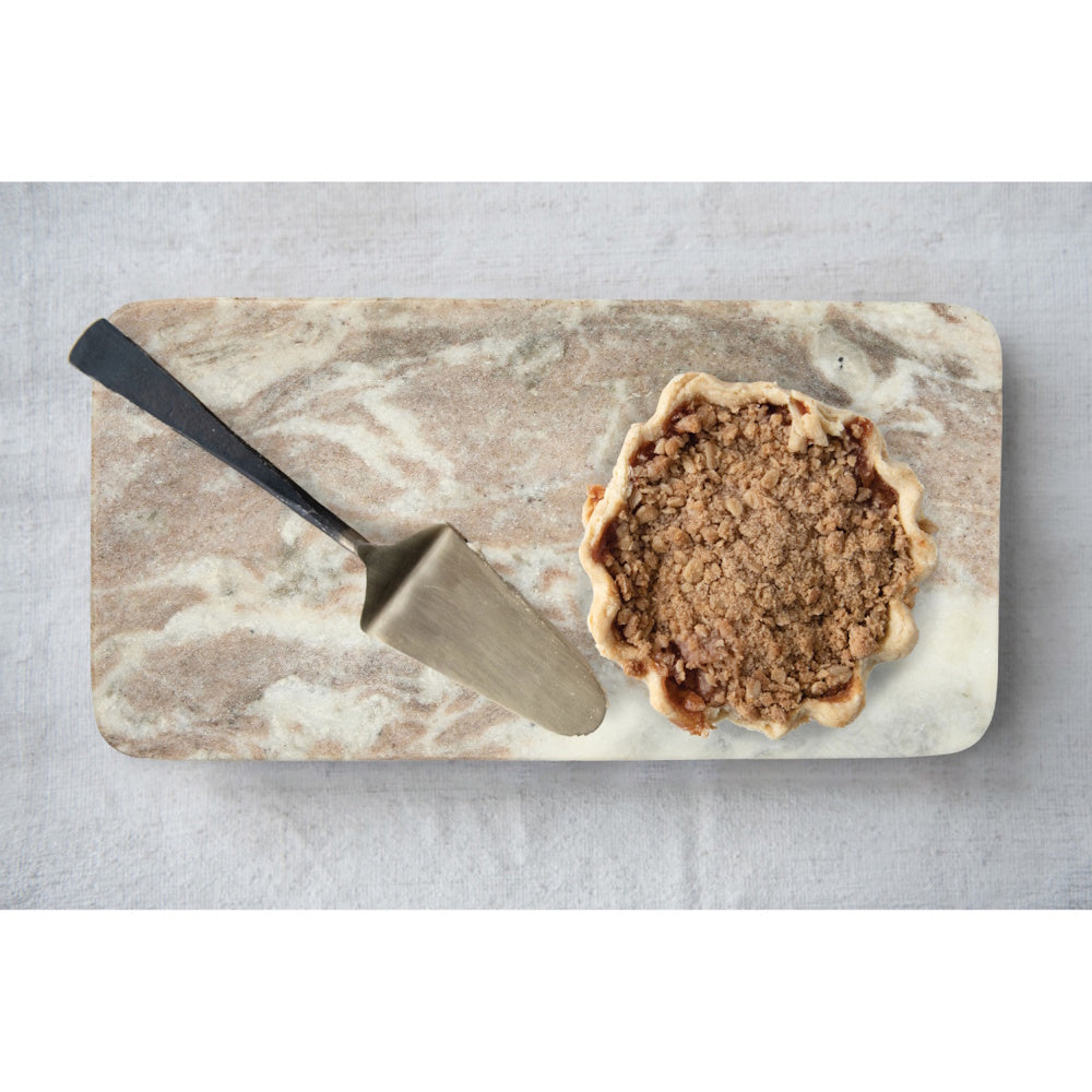 Overhead view of a small crumble pie and a metal server on a rectangular, marbled beige serving board.