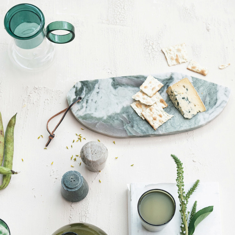 Overhead view of stone salt and pepper shakers next to a marble board with cheese, crackers, and glassware.