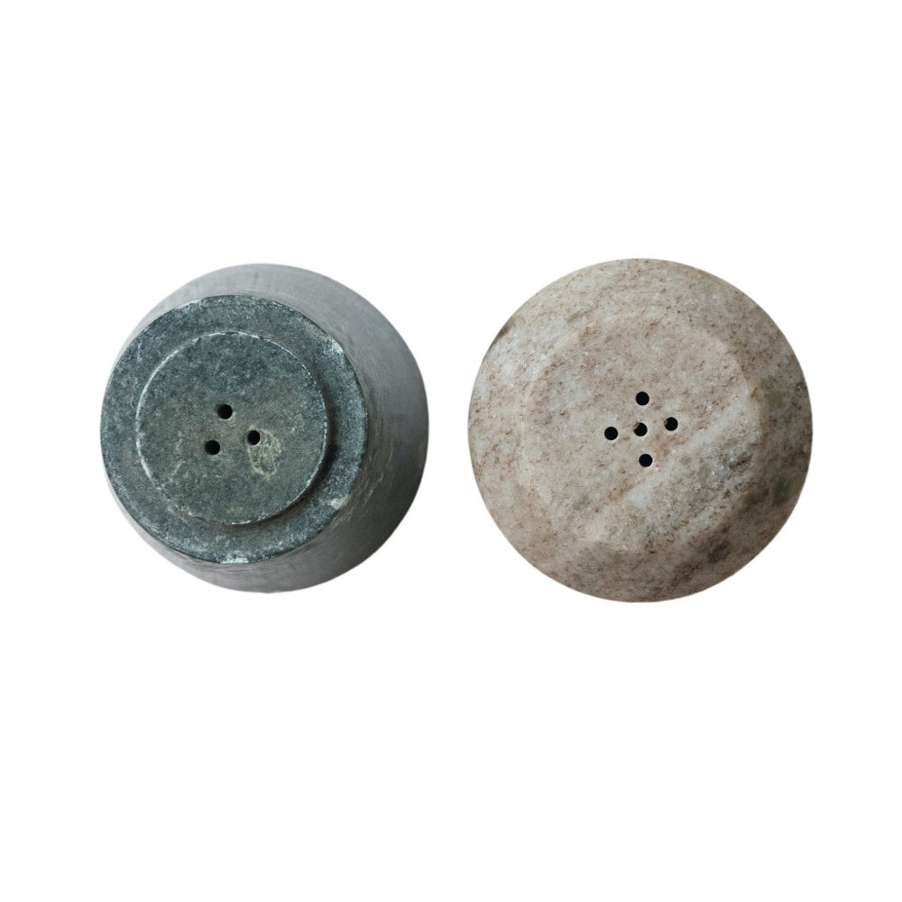 Top-down view of two marble shaker pieces; a dark green piece with three holes and a light grey piece with five.