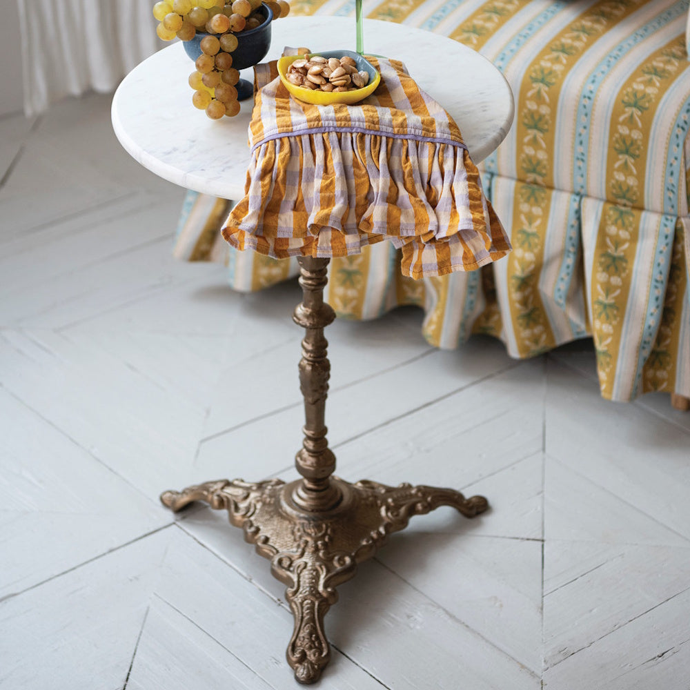 Round white marble top side table with an ornate antique brass cast iron pedestal base in a living room.