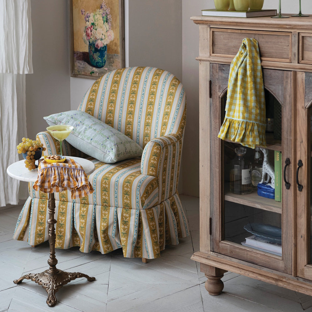 Marble topped side table with cast iron base next to a striped armchair.