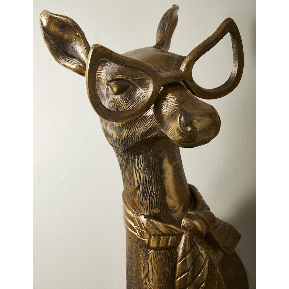 Bronze deer wall mount wearing large cat-eye glasses and a scarf, captured in a close-up shot against a plain wall.