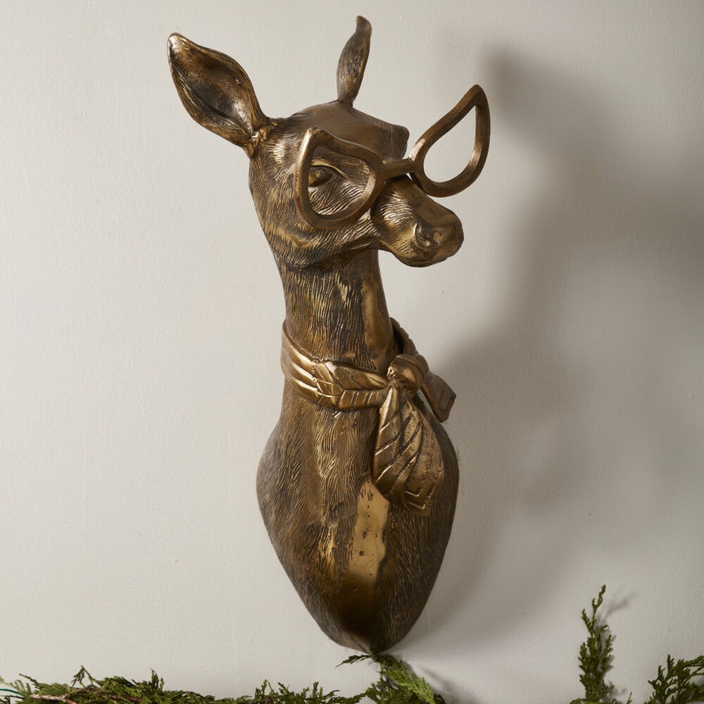 Bronze-toned deer bust wall mount wearing cat-eye glasses and a patterned neck scarf, viewed from the side.