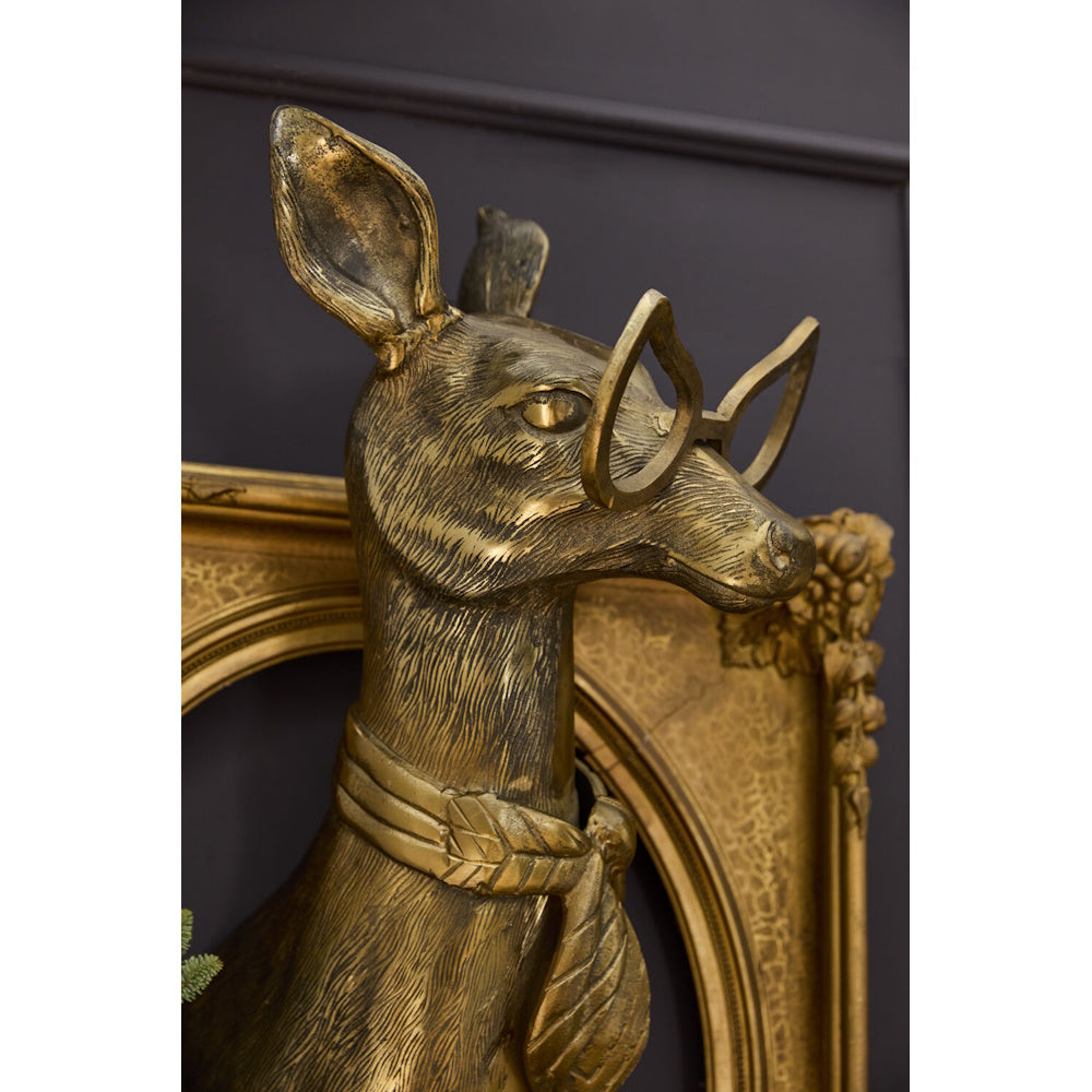 Gold deer sculpture bust wearing glasses and a scarf, mounted on a dark wall inside an ornate gold frame.