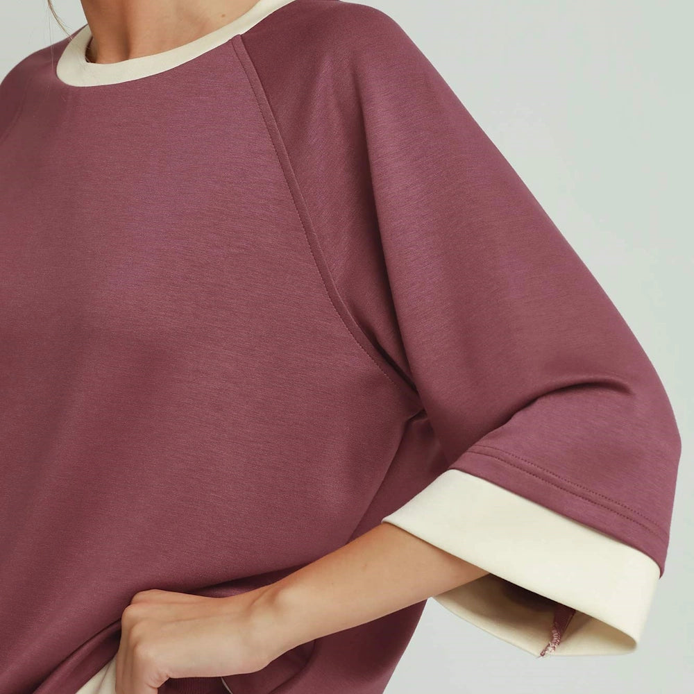 Close-up of a mauve knit top featuring raglan sleeves with contrasting cream collar and cuff trim.