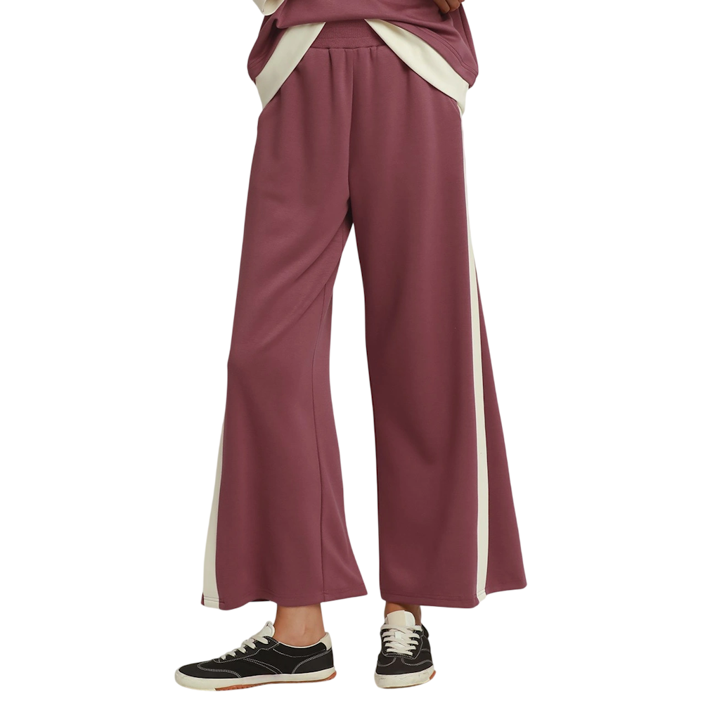 Woman wearing mauve wide-leg knit pants with cream side stripes and dark sneakers.