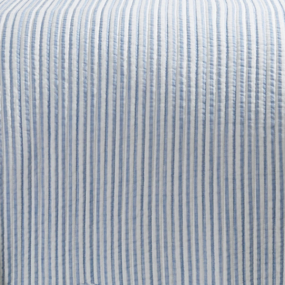 Close-up view of light blue and white striped quilted fabric texture and channel stitching.