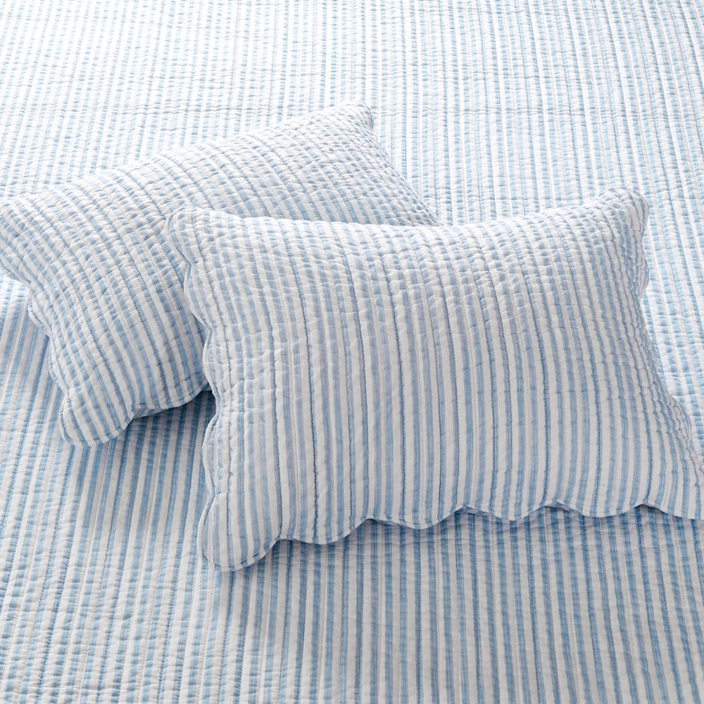 Two light blue and white striped quilted pillow shams with scalloped edges resting on a matching quilt.