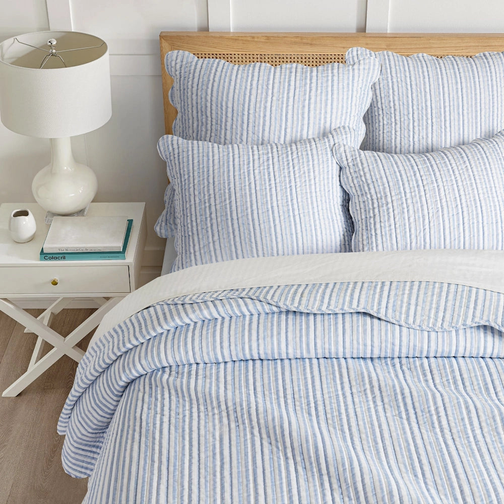 Top-down view of a bed with light blue and white striped quilt and matching scalloped pillow shams.