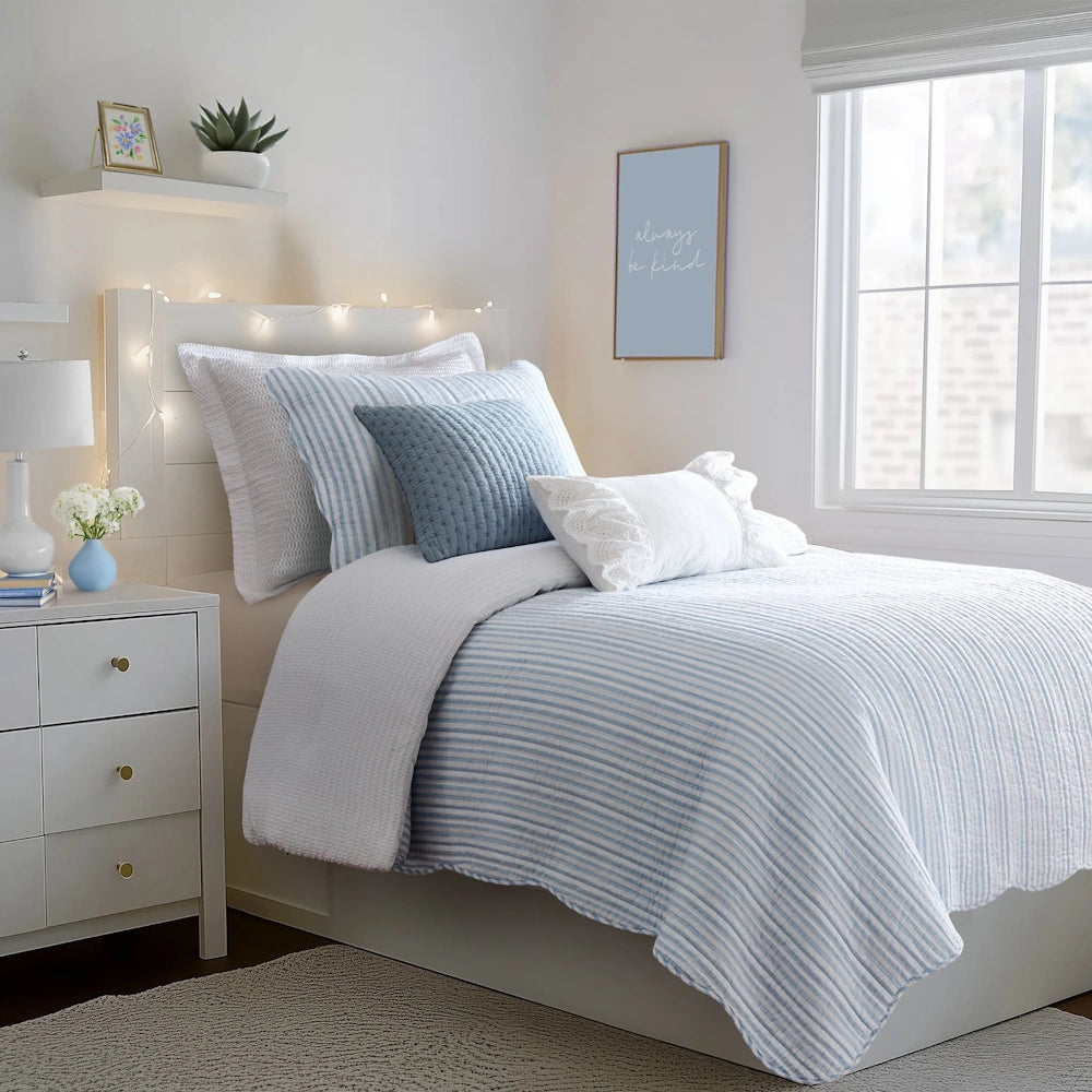 Bed dressed in a blue and white striped quilt set with matching shams and throw pillows in a bedroom.