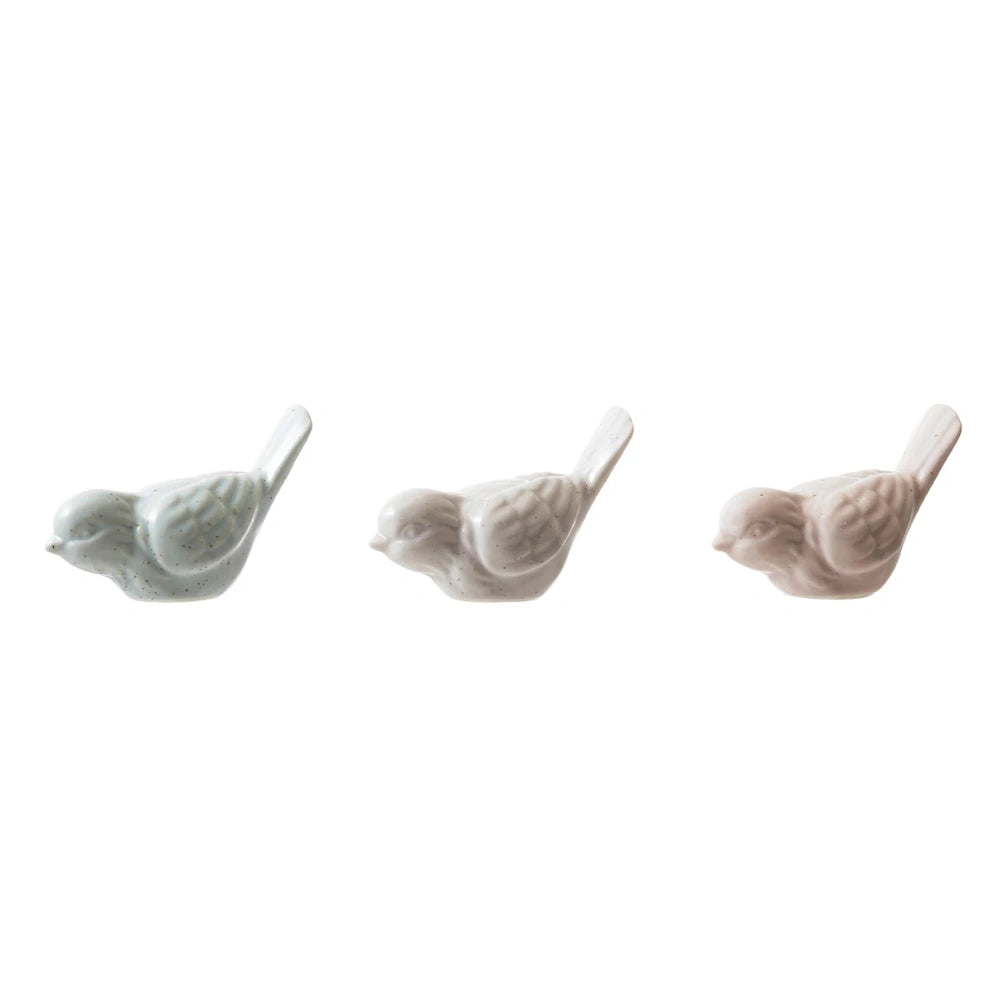 Three matte-finish stoneware bird figurines in muted blue, grey, and pink tones on a white background.