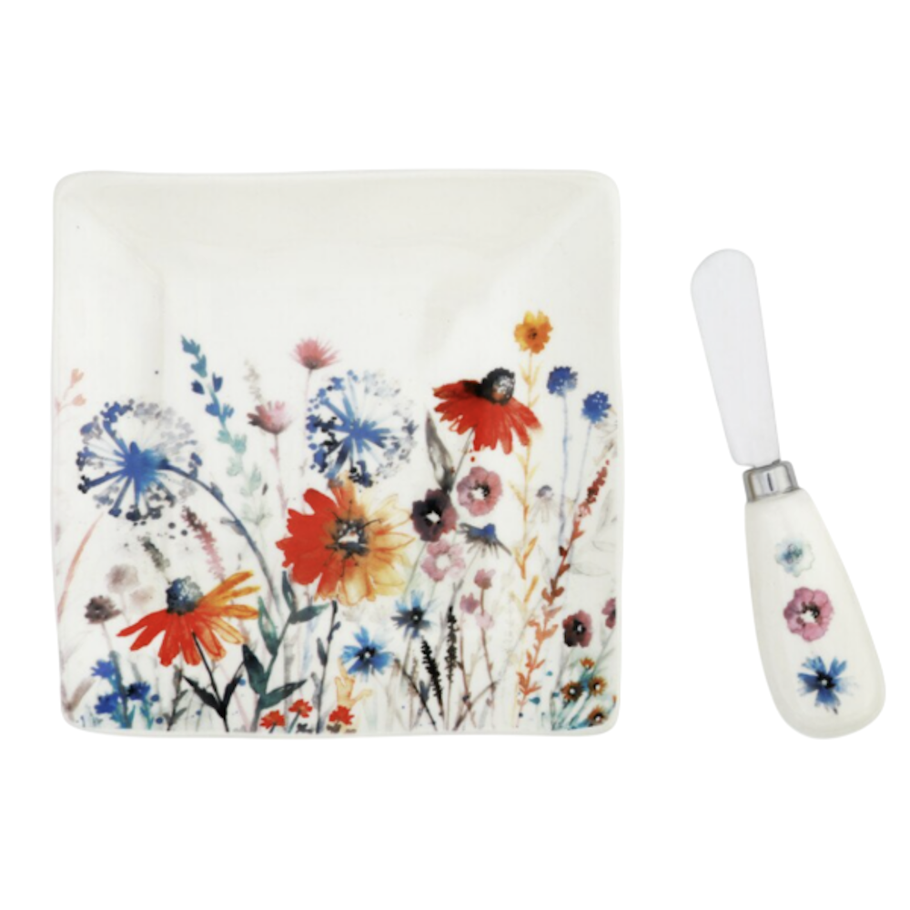 A square white dish with a colorful wildflower pattern, next to a matching floral-handled spreader knife.