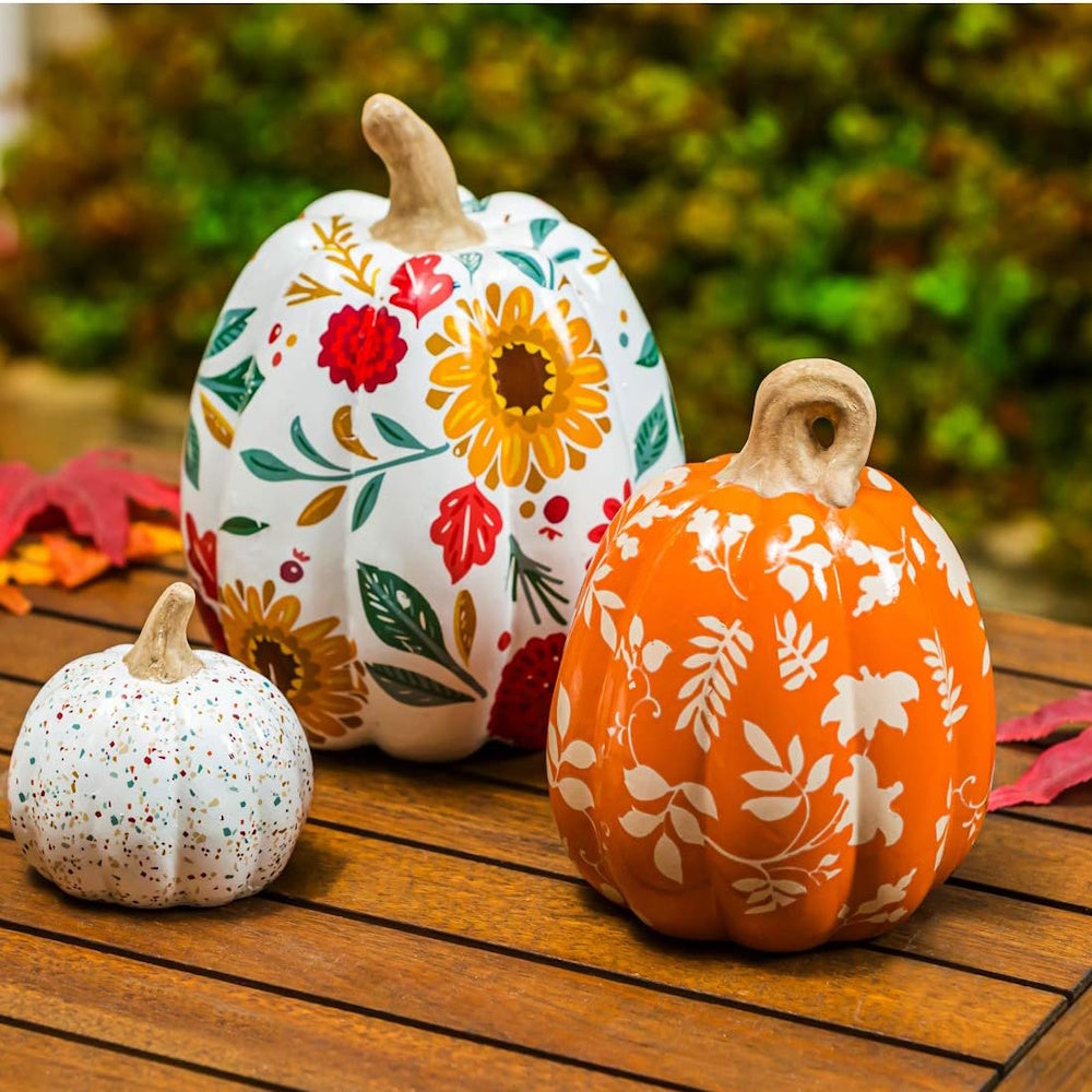 Three decorative ceramic pumpkins with autumn floral patterns and speckles on a wooden table.