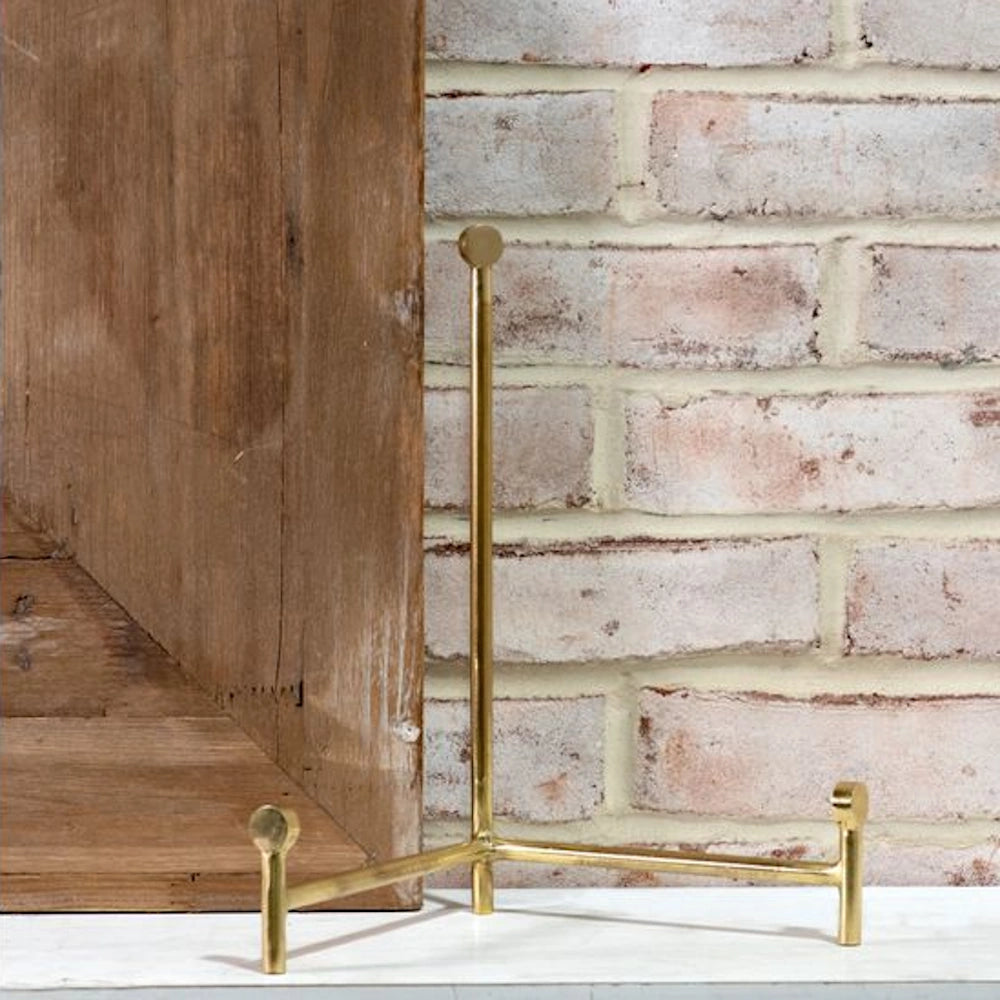A minimalist gold brass decorative display stand, featuring three round feet and a T-bar upright post.