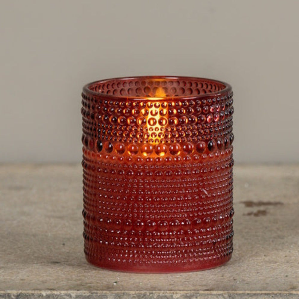 Burgundy dotted glass candle glowing warm light on a rustic stone surface.