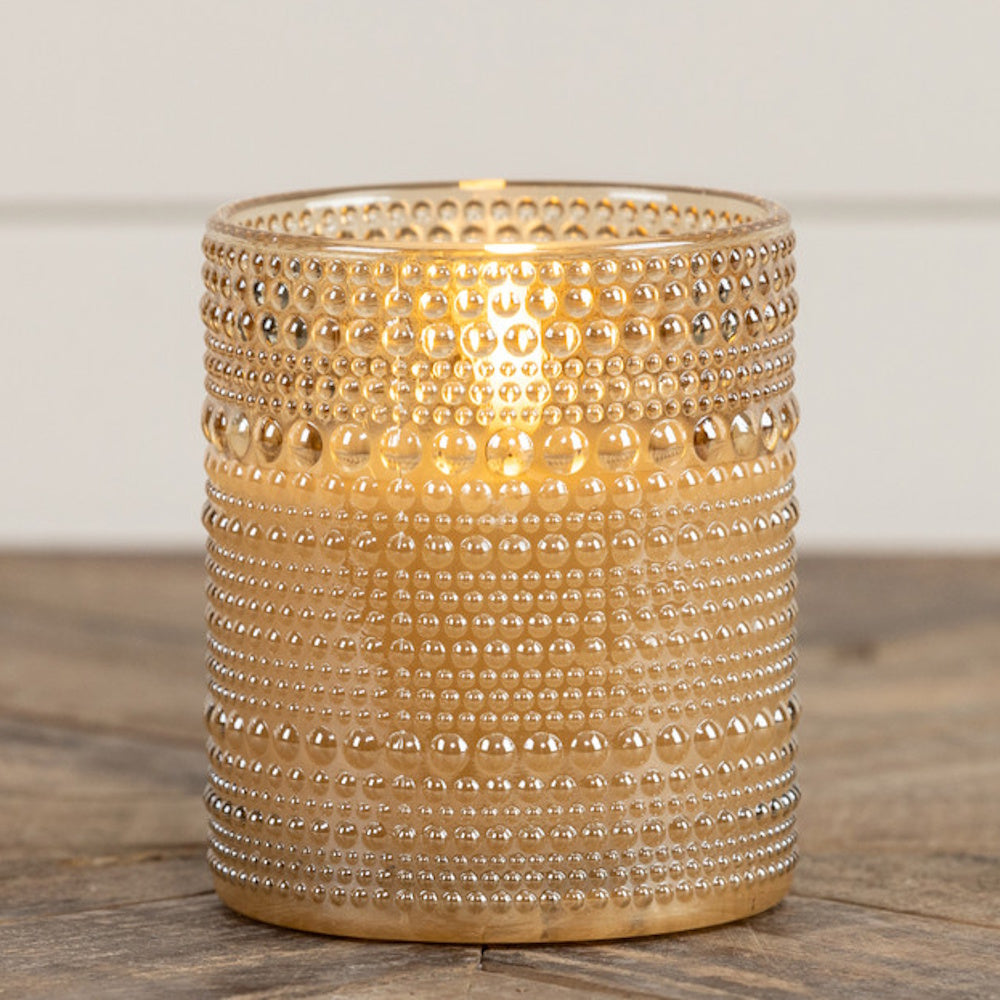 Champagne-tinted hobnail glass candle holder glowing with a warm warm light inside.