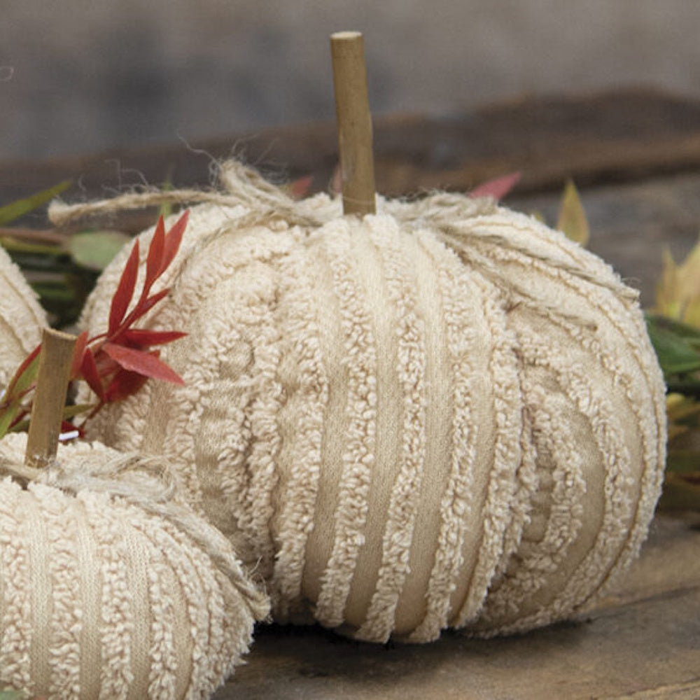 Cream chenille fabric pumpkin with wooden stem and jute twine bow on wooden surface.