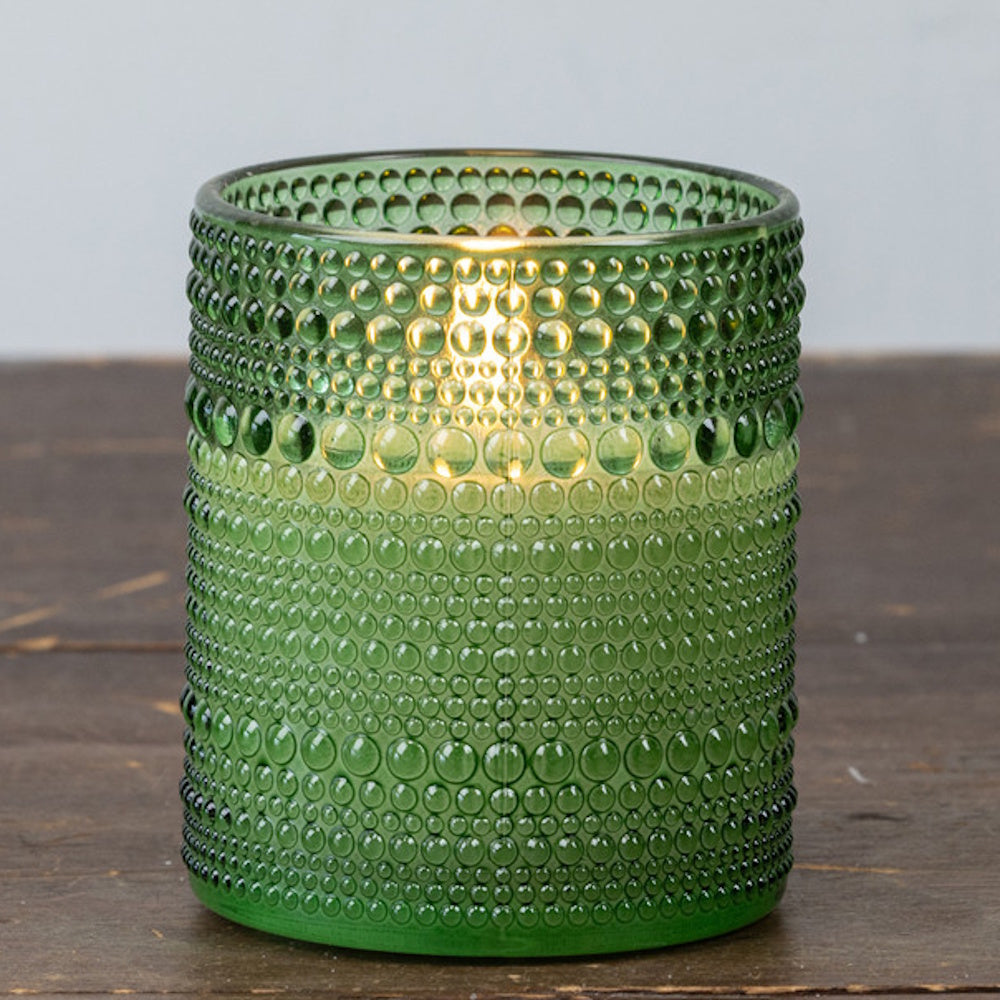 Lit green beaded glass candle holder sitting on a wooden surface.