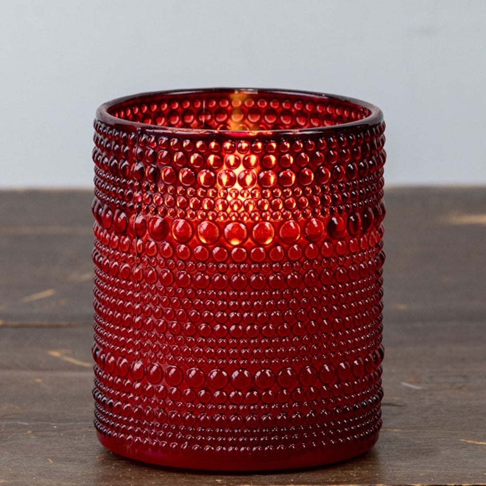 Lit red beaded glass candle holder sitting on a wooden surface.