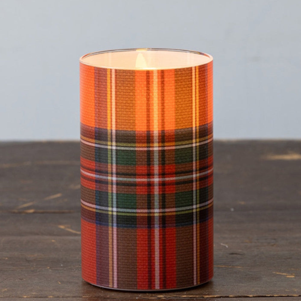 A glowing flameless pillar candle with a red tartan plaid pattern on a rustic wooden surface.
