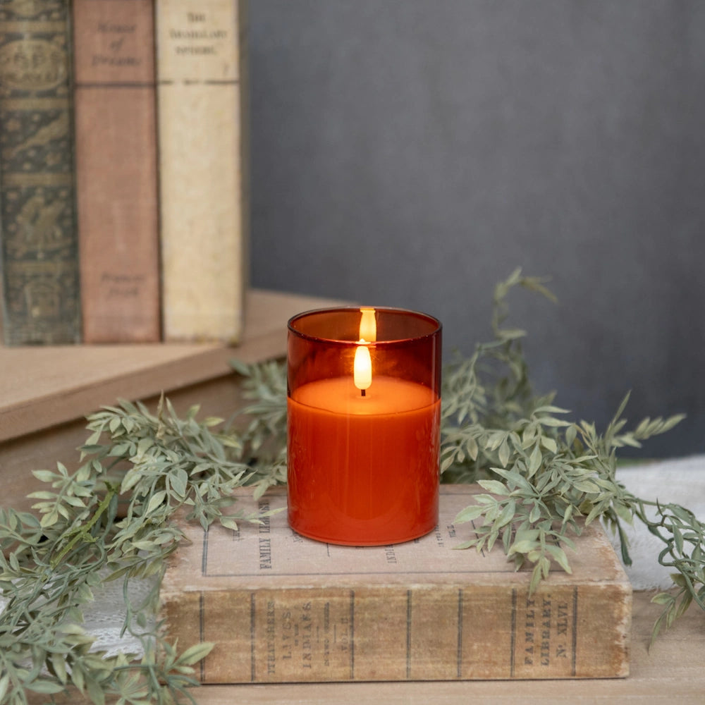 Glowing sienna glass flameless candle resting on a vintage book with leafy greenery.