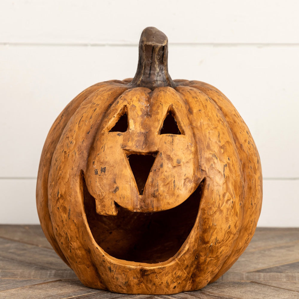 Textured terracotta jack-o'-lantern with a carved wide open smile sitting on a wooden surface.