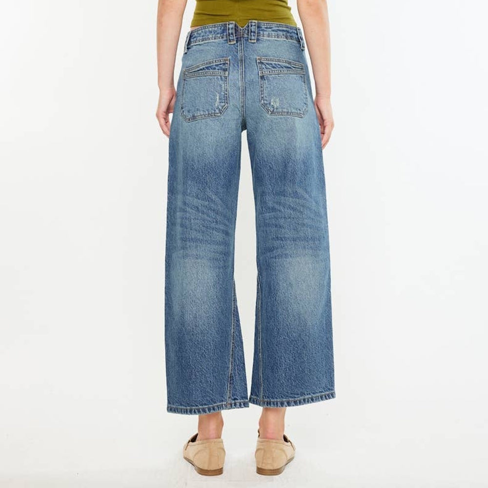 Rear view of a person wearing loose medium-wash barrel-leg jeans with back patch pockets and beige loafers.