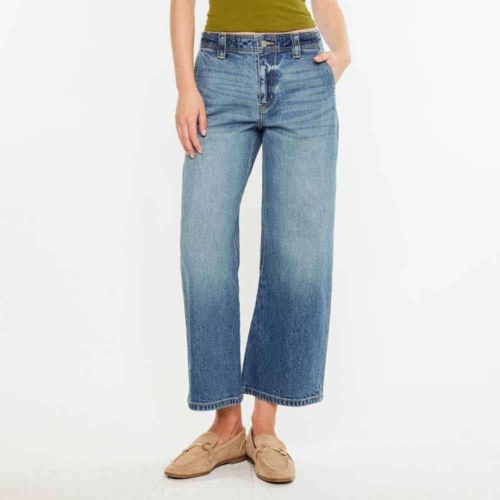 Front view of medium-wash loose barrel-leg jeans styled with a green top and beige suede loafers.