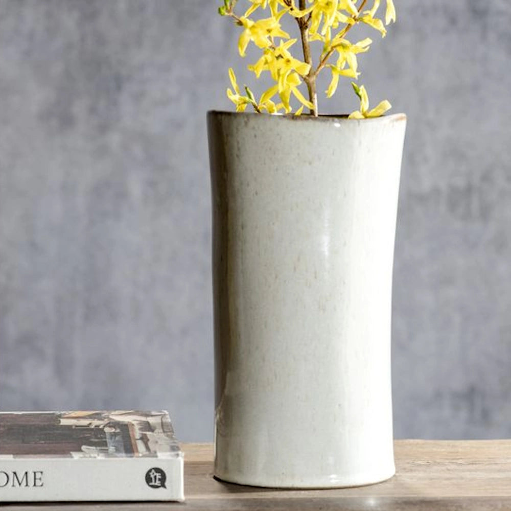 White sand ceramic vase with yellow flowers on a wooden table, minimalist home decor against a grey stone wall.