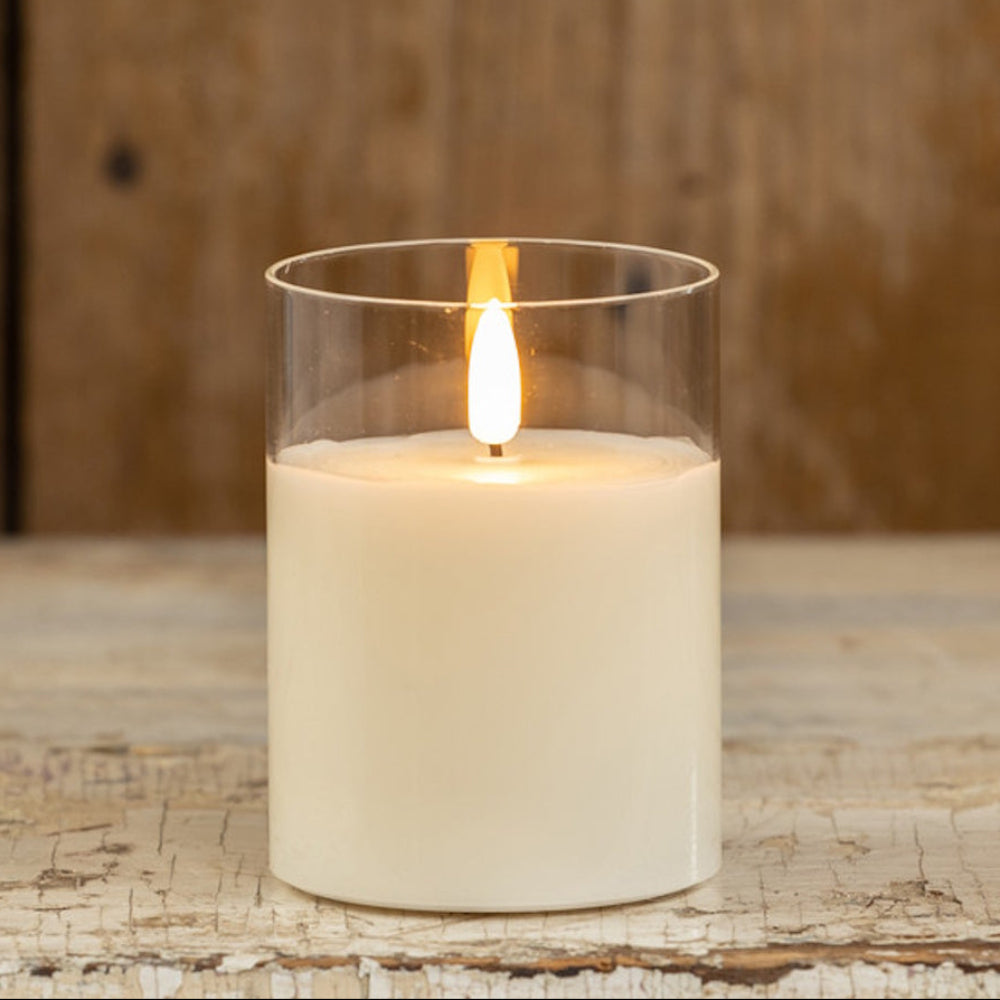 Lit flameless white candle in a clear glass cylinder against a rustic wooden background.