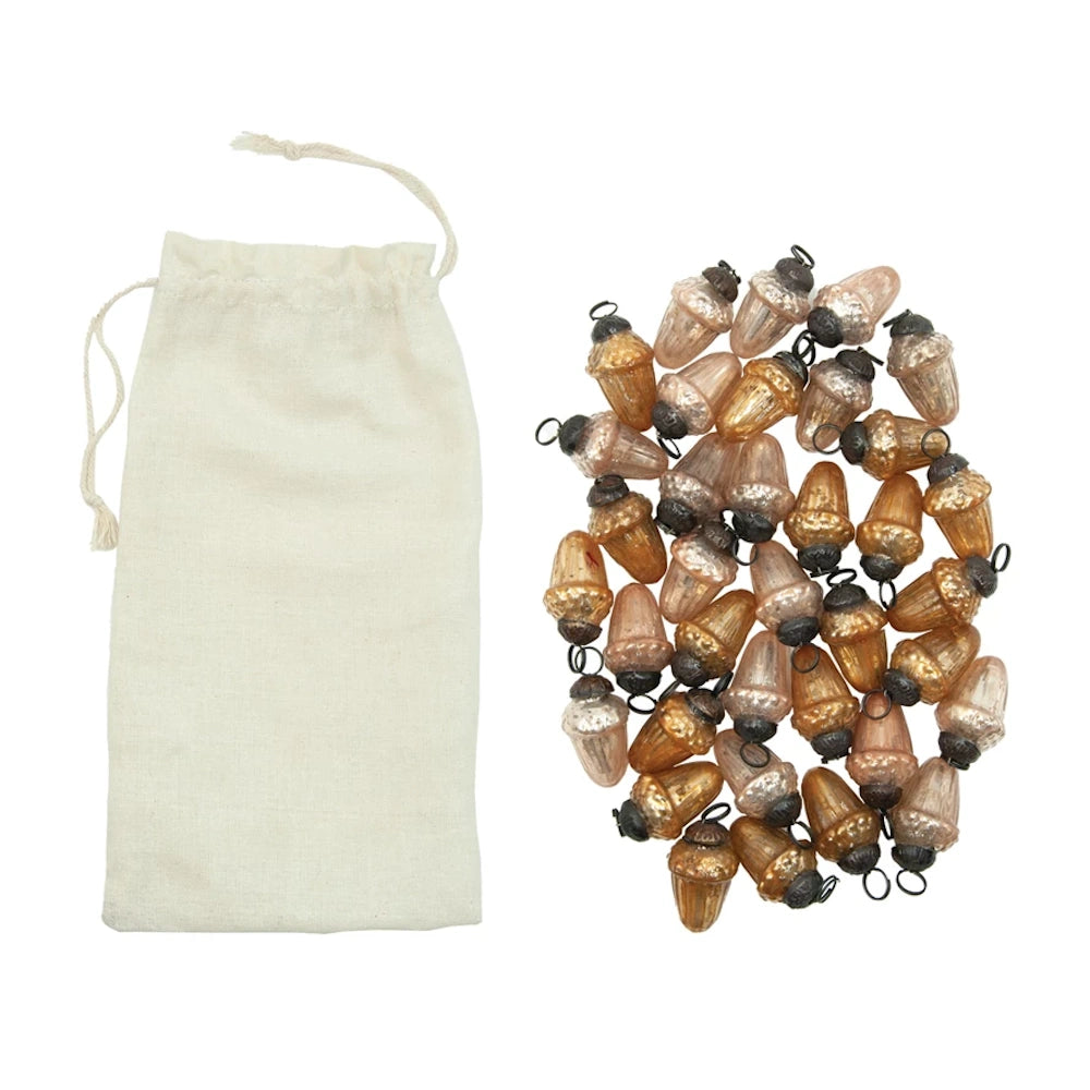 Mercury glass acorn ornaments in shades of gold and silver next to a white fabric drawstring storage bag.