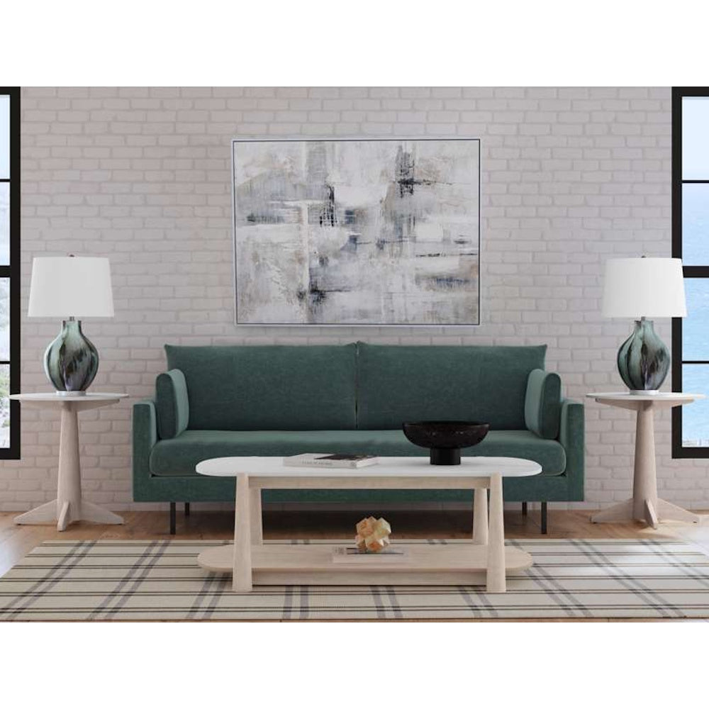 Modern living room with a teal sofa, white coffee table, and abstract wall art against a white brick wall.