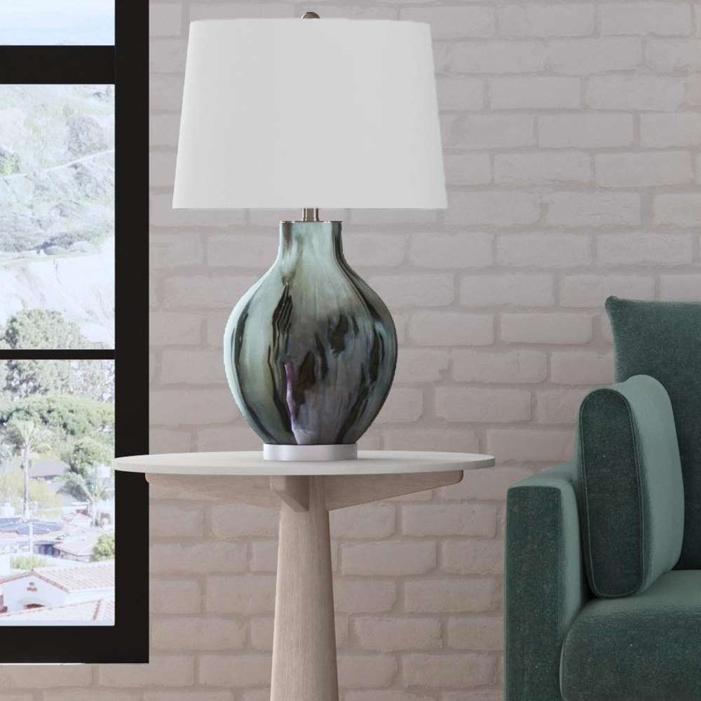 Modern table lamp with a marbled glass base and white drum shade, set on a side table in a living room.
