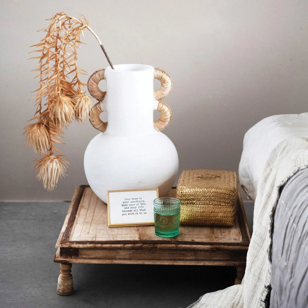 Small gold easel frame with inspirational quote on a rustic wooden table next to a white ceramic vase and woven basket.