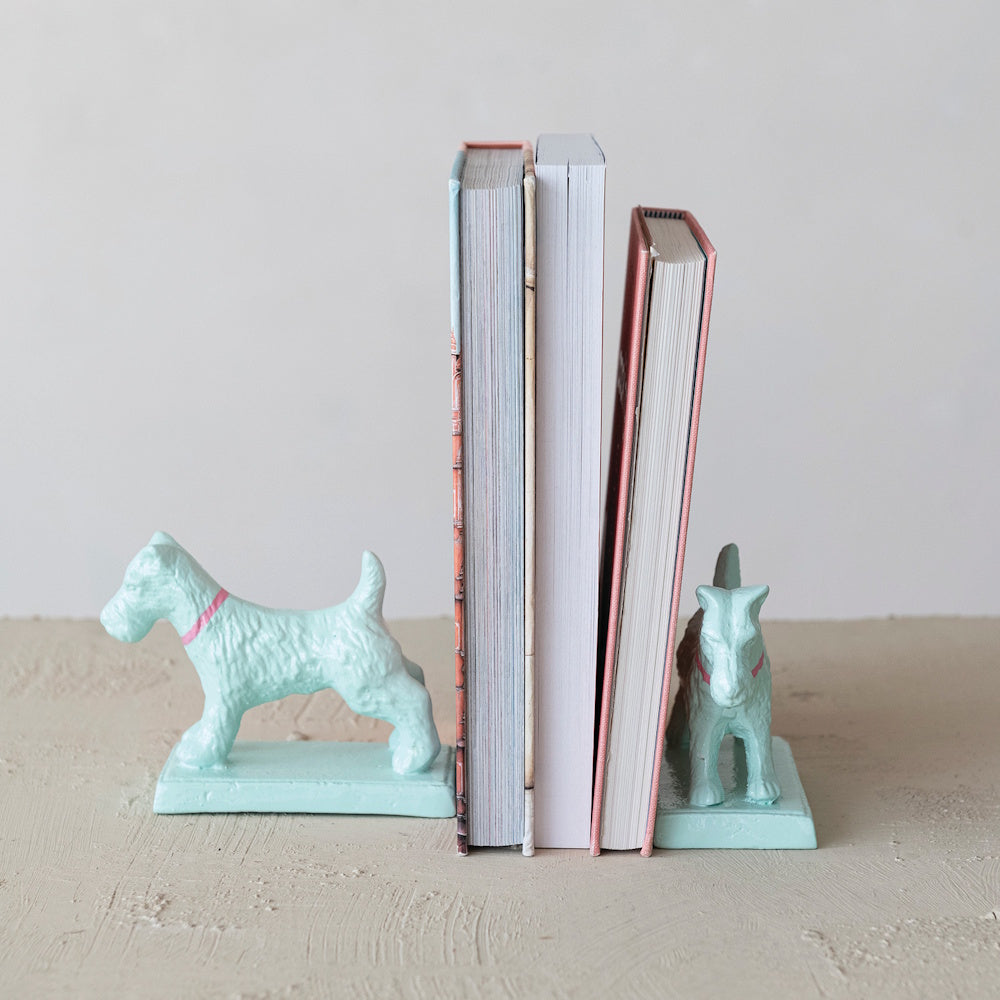Three upright books held together by a pair of mint green metal dog bookends on a textured surface.