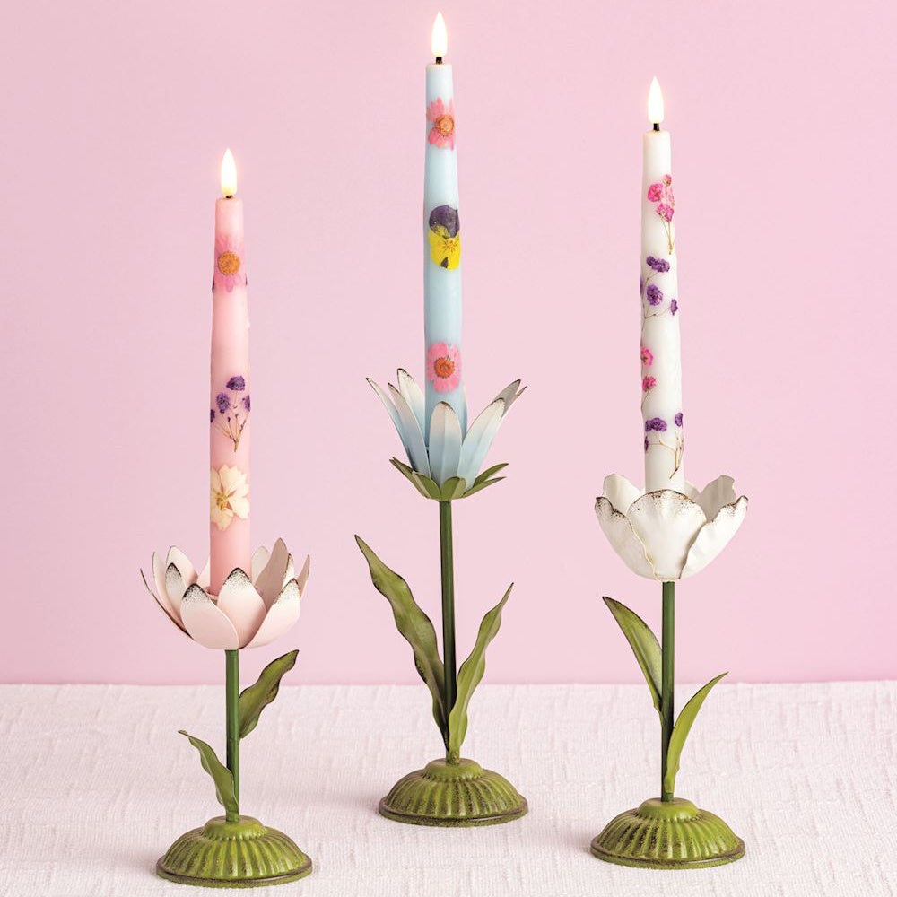 Three metal flower taper candle holders with floral-patterned candles on a pink background.