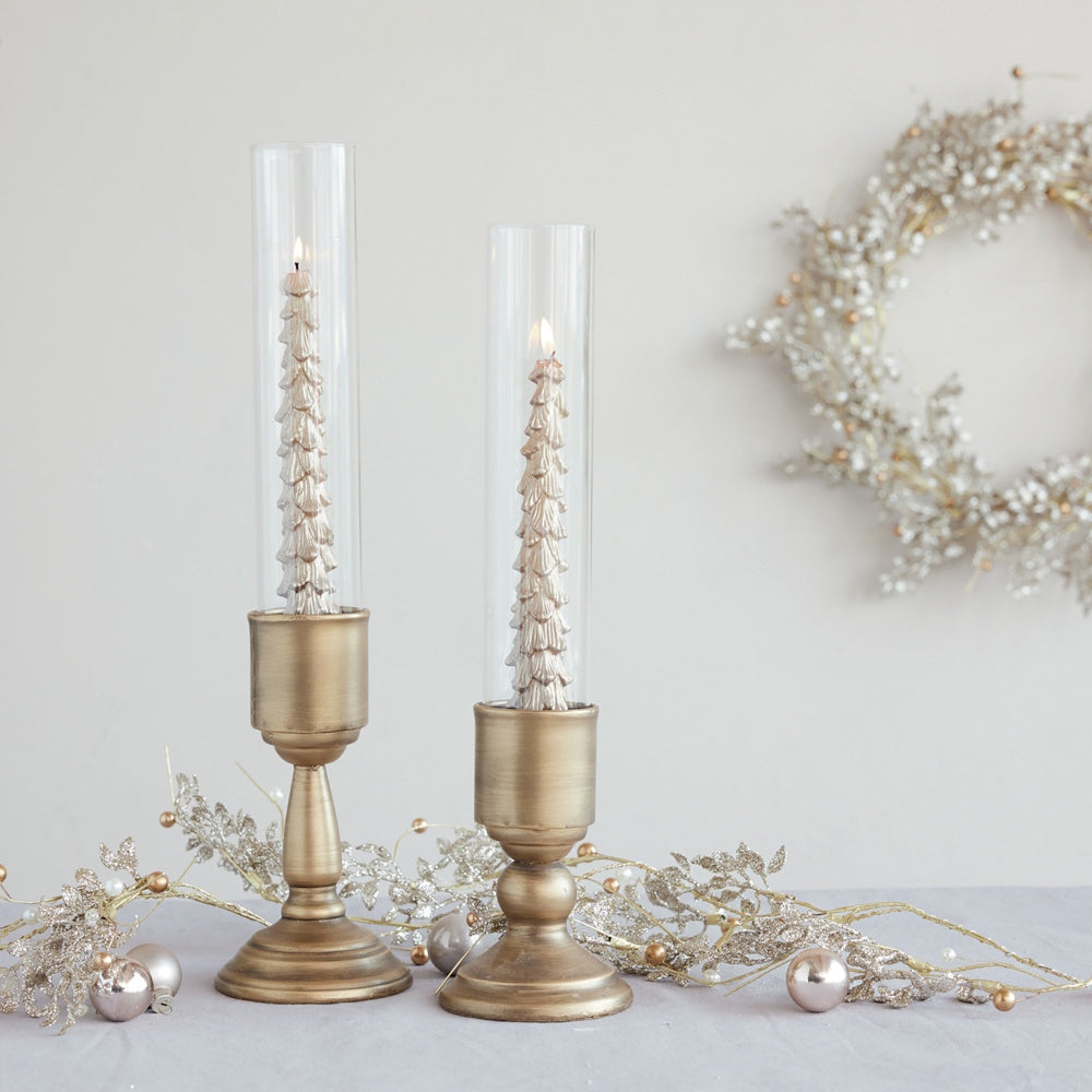 Gold metal taper candle holders with glass hurricane shades holding tree-shaped candles.