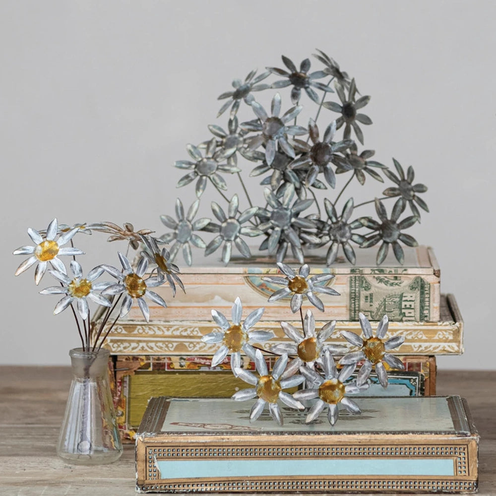 Metal vintage-style daisy decorations displayed in a glass vase and styled on decorative antique boxes.
