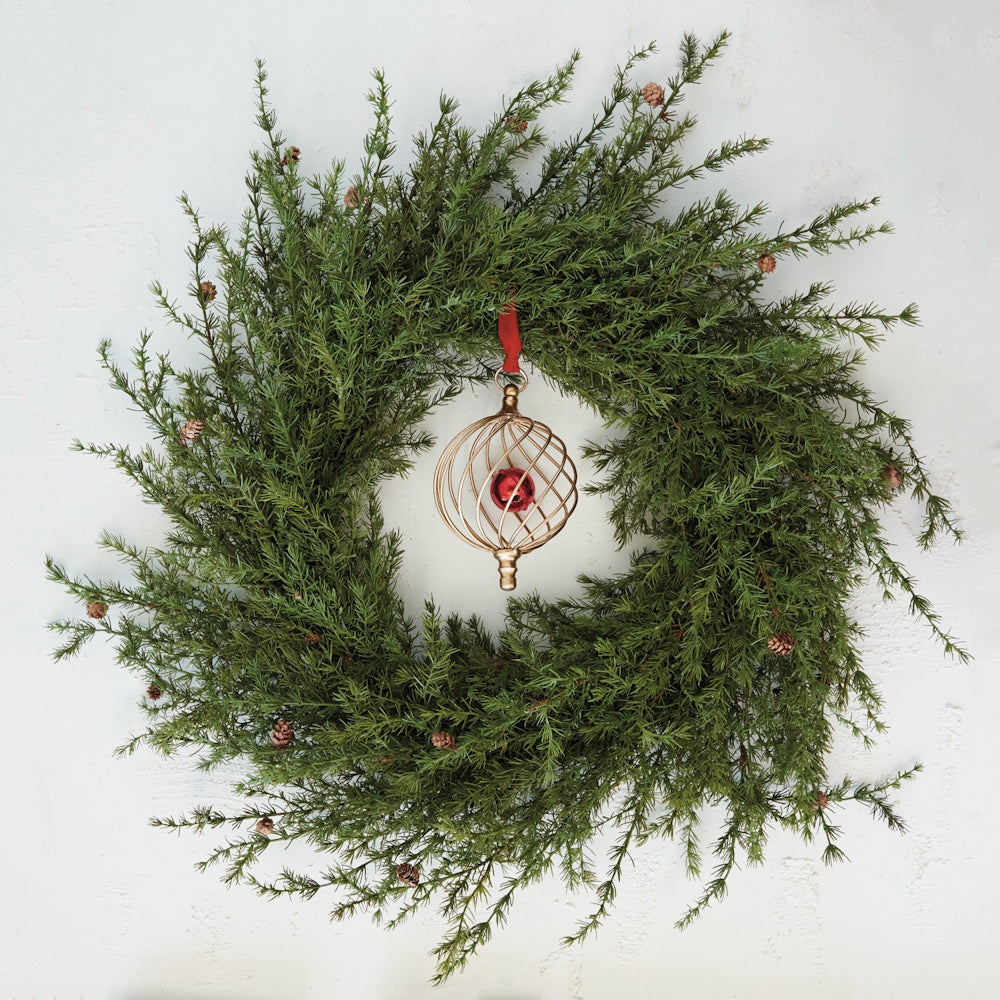 Gold wire frame ornament with an inner red bell, hanging inside an evergreen Christmas wreath.