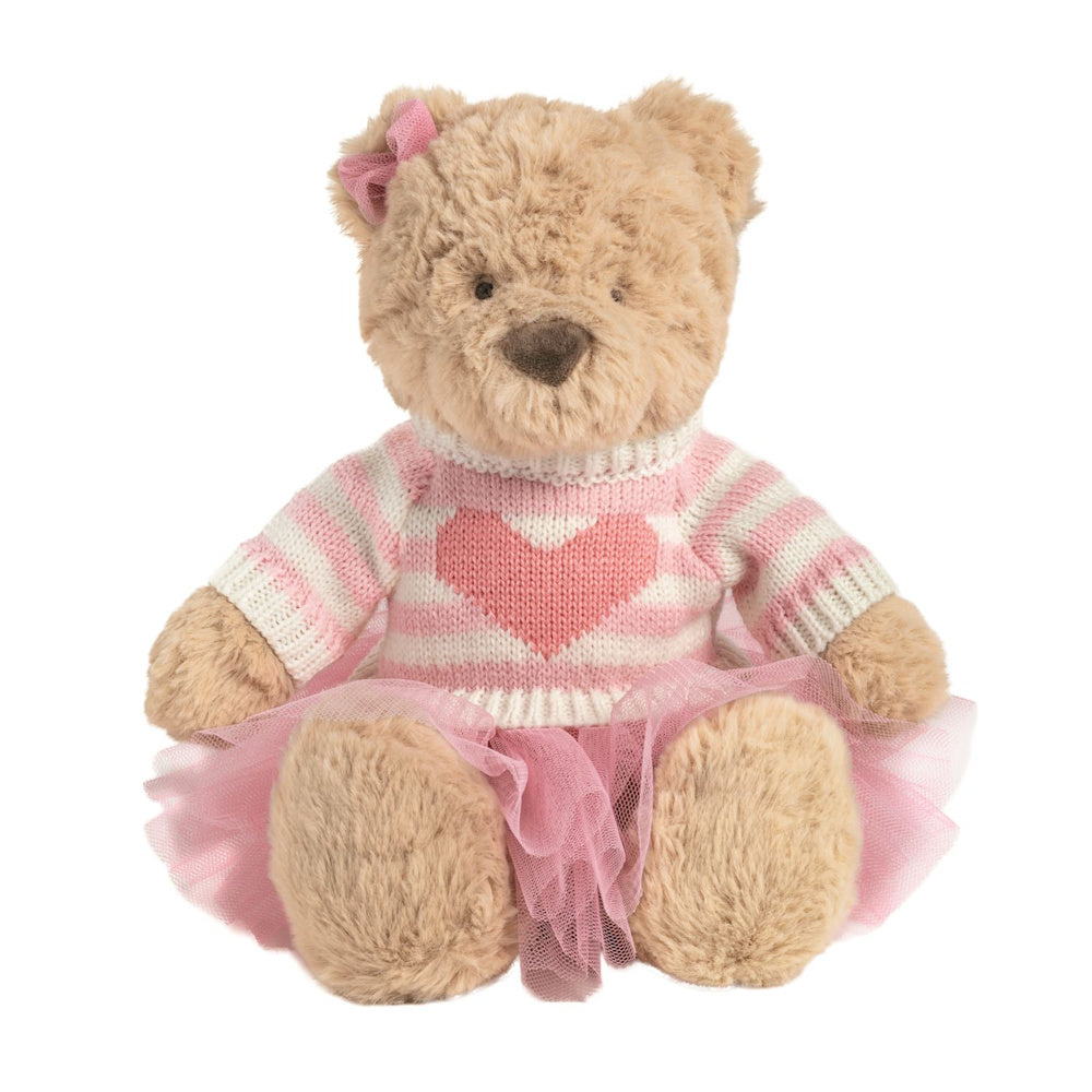 Plush tan teddy bear wearing a pink striped heart sweater and tutu with a pink bow on its ear on white background.