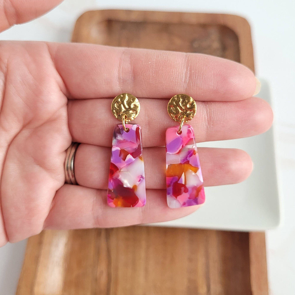 Pink and orange tortoiseshell acetate drop earrings with hammered gold studs, held in a hand for scale.