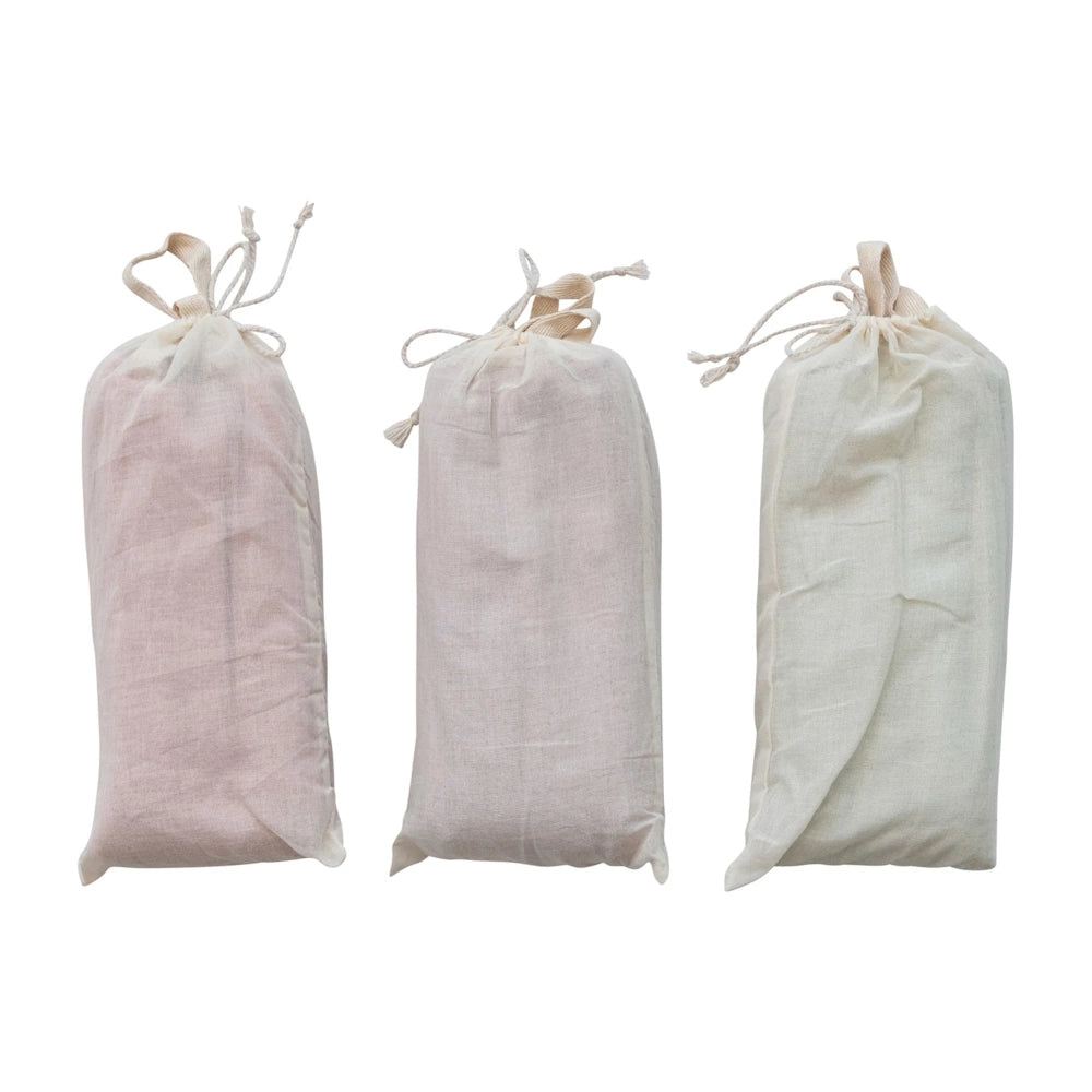 Three fabric drawstring pouches in pink, mauve, and cream containing microwavable hot and cold neck wraps for pain relief.