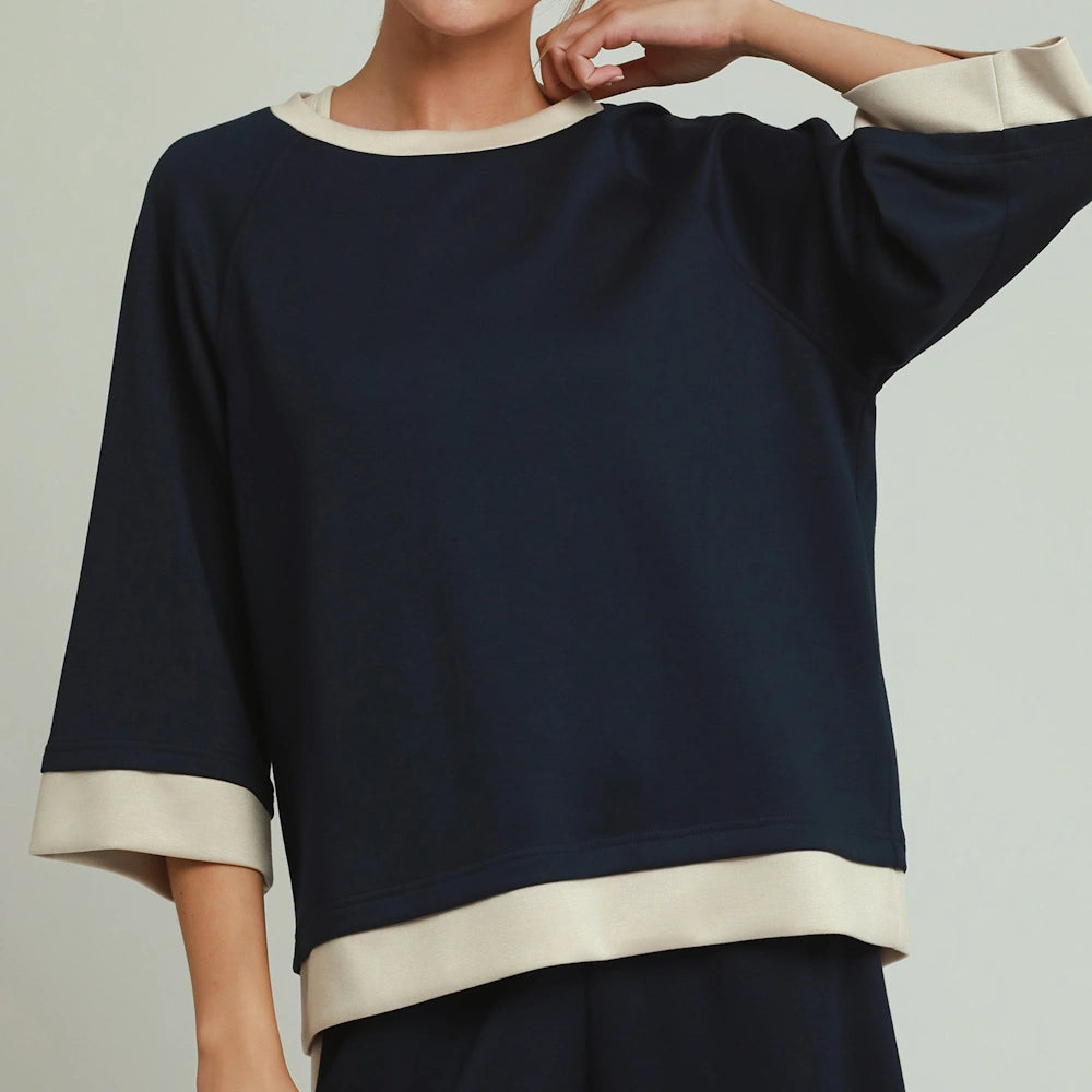 Midnight blue crewneck top with beige contrast trim on the collar, sleeve cuffs, and hem.