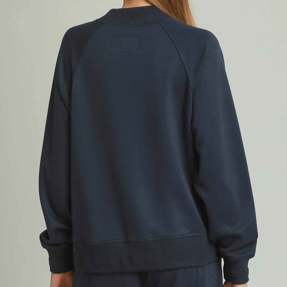 Back view of a woman wearing a midnight blue mockneck pullover sweater with ribbed trim.