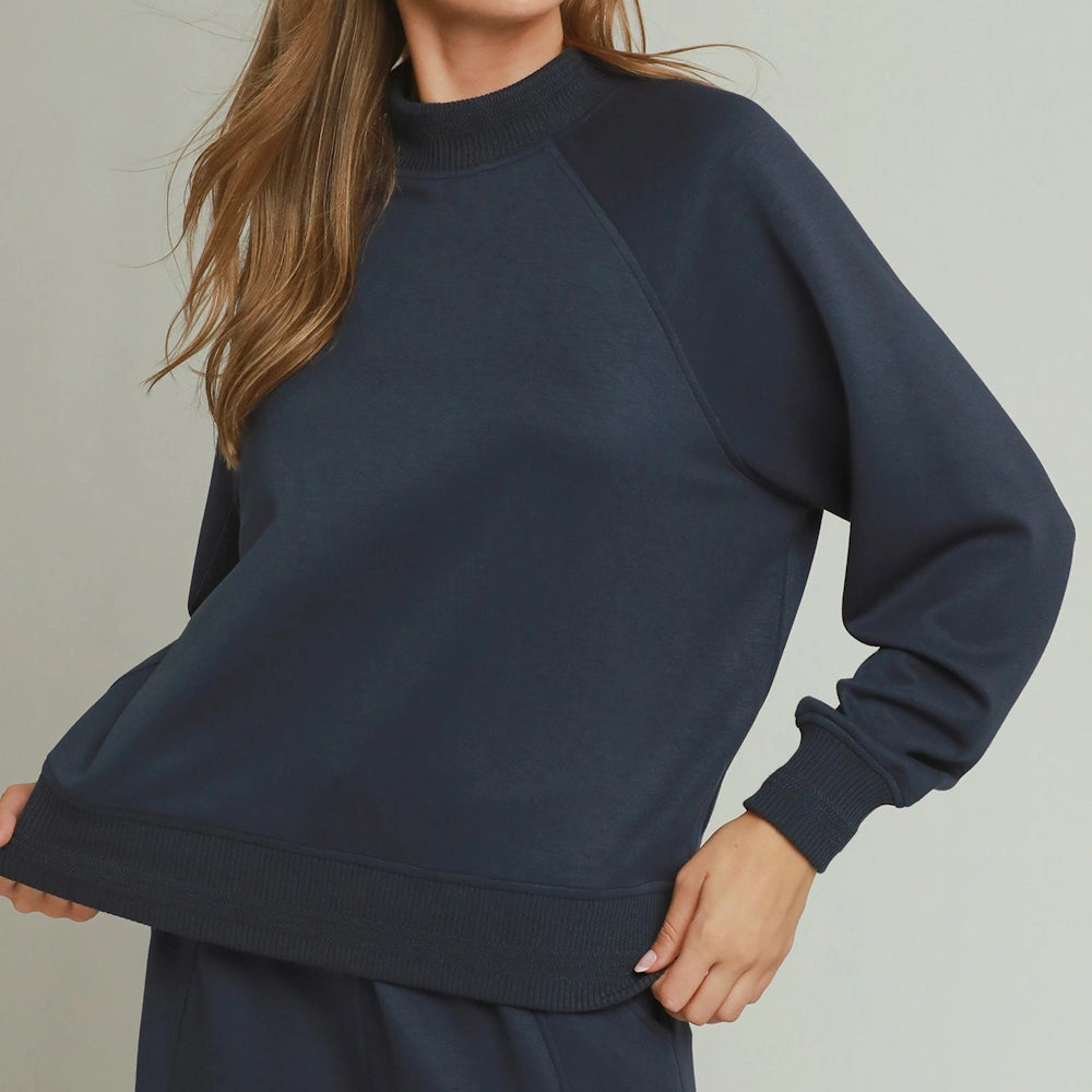Woman wearing a midnight blue mockneck pullover sweater with ribbed cuffs and hem.