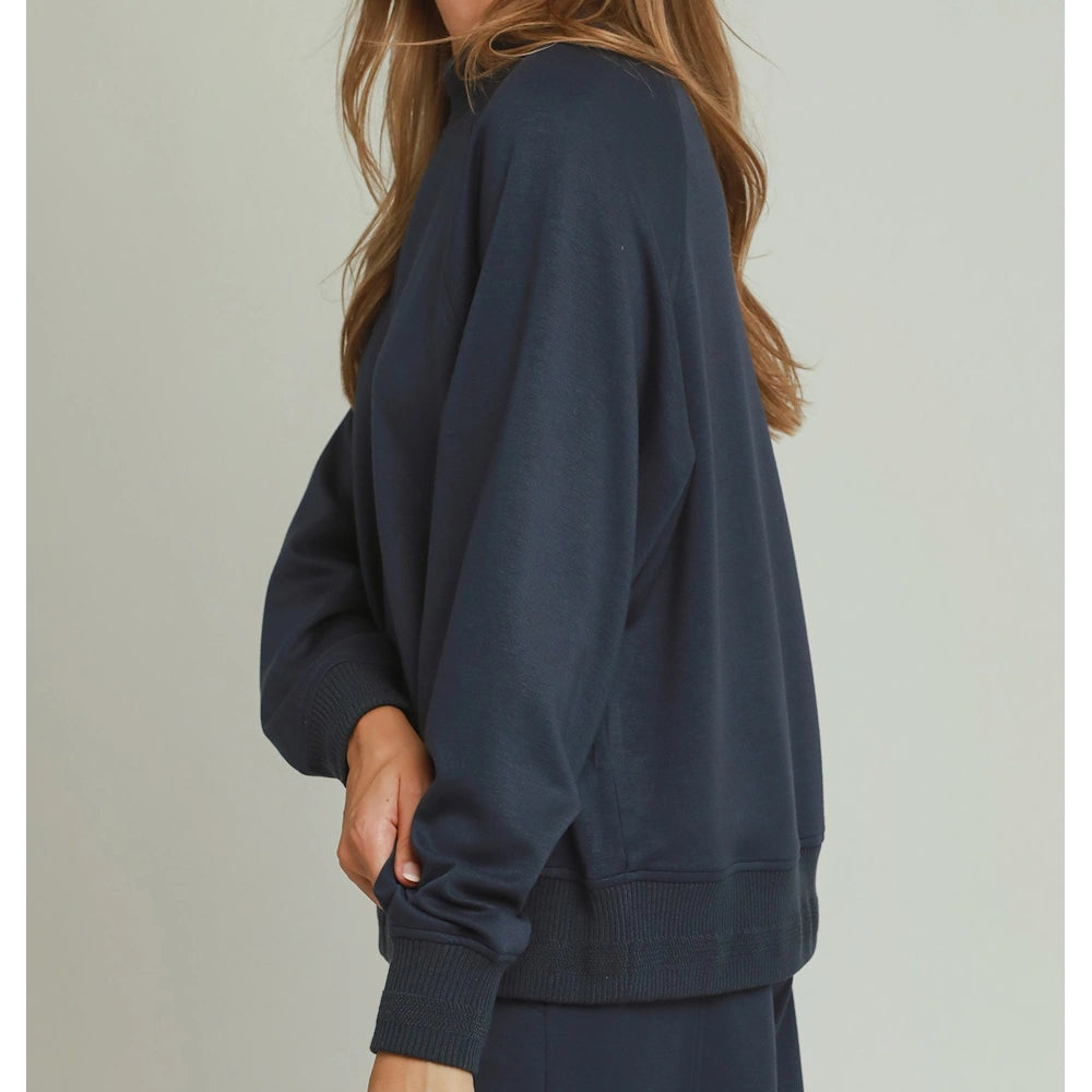 Side profile of a woman wearing a dark blue mock-neck long-sleeve sweater with ribbed cuffs.
