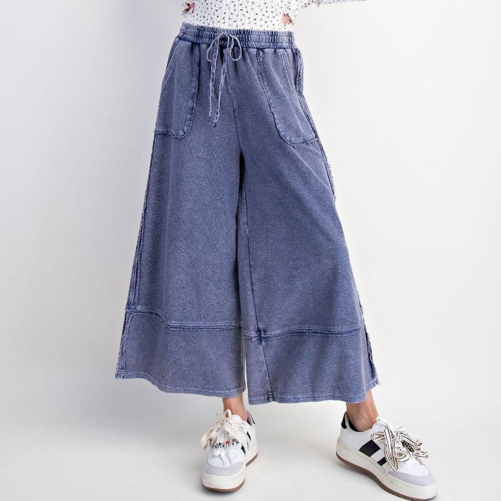 Midnight blue mineral wash palazzo pants with drawstring waist, wide leg, and pockets, styled with white sneakers.