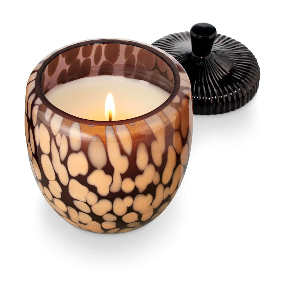 Lit scented candle in an acorn-shaped glass jar with a tortoiseshell pattern and its lid next to it.