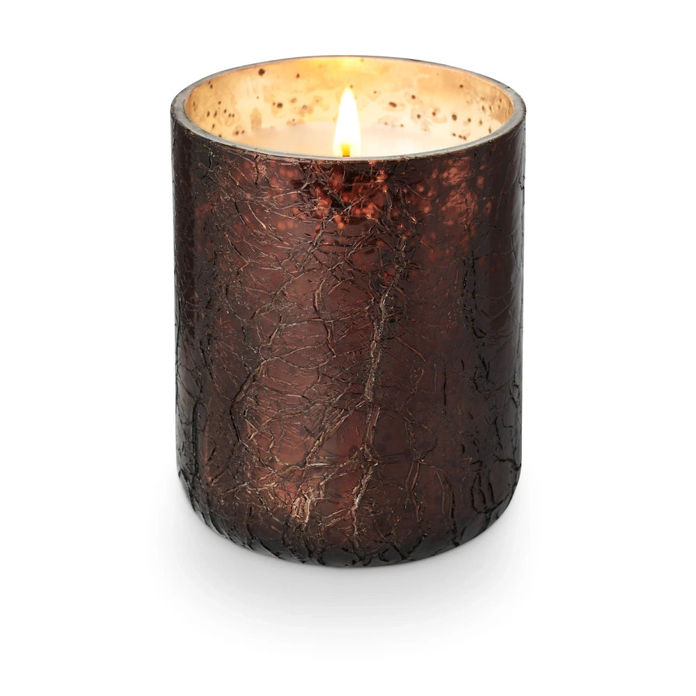 Lit scented candle glowing inside a dark brown, textured crackle glass jar against a white background.
