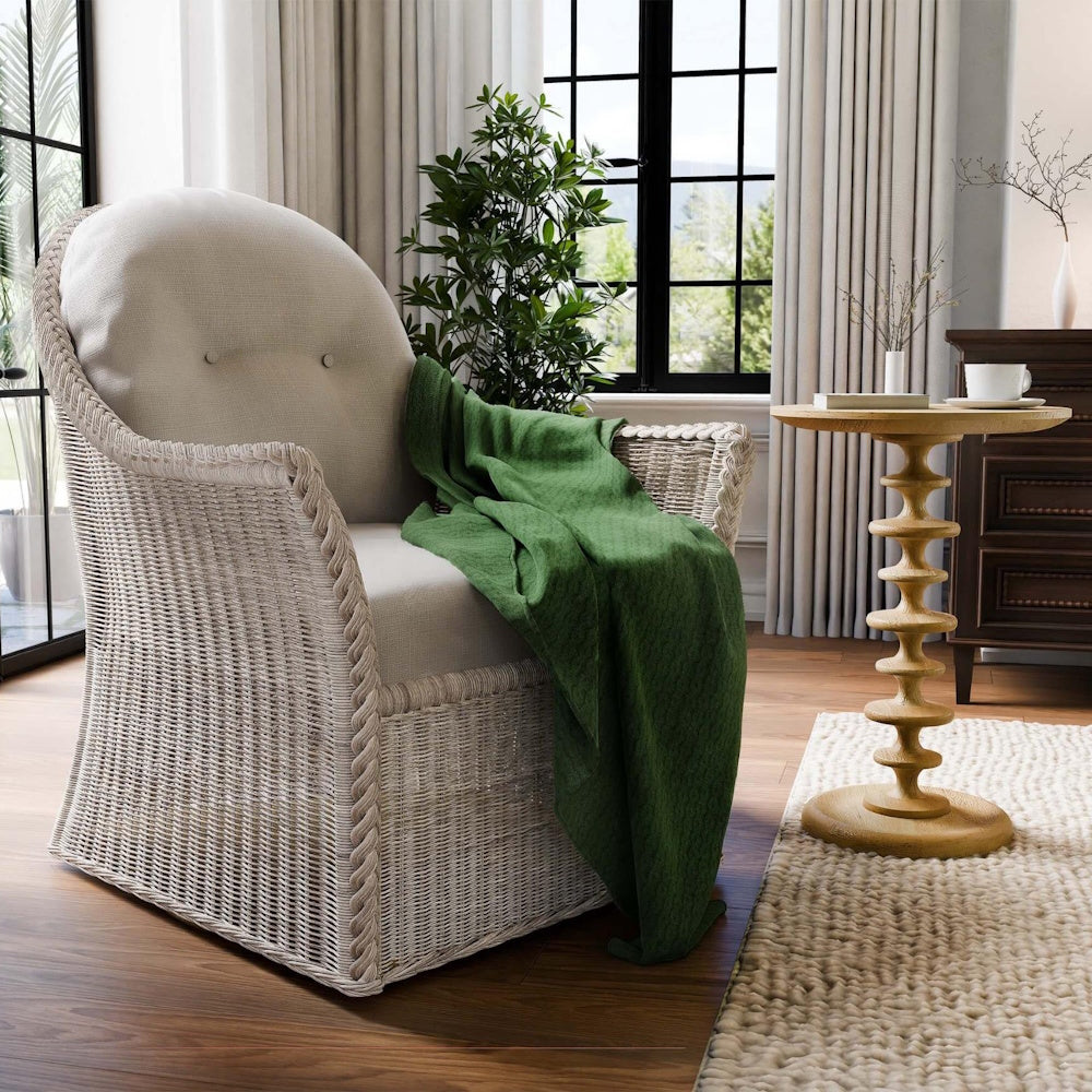 Wicker armchair with a green blanket next to a Milano round wooden side table in a bright room.